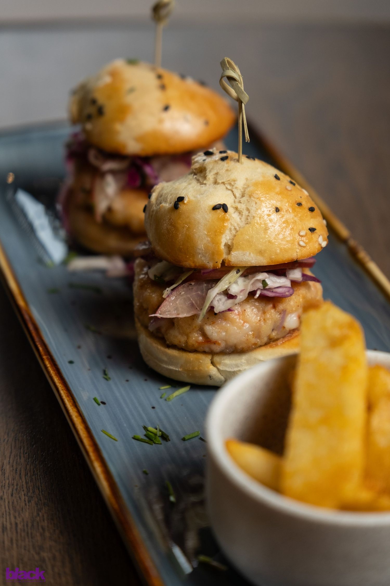 Gourmet mini burgers with black sesame seeds served alongside golden french fries.