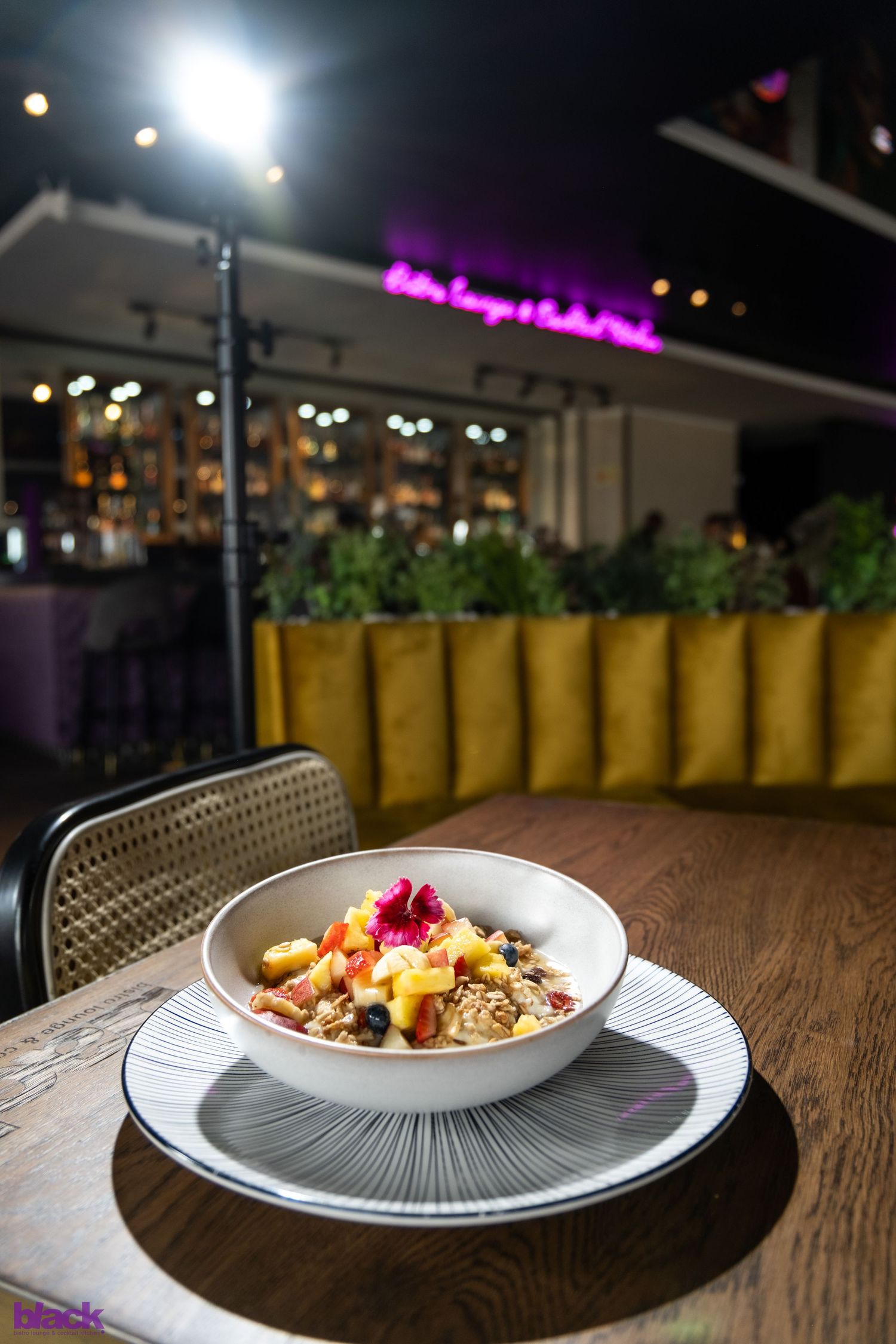 Artfully plated breakfast bowl with fruit garnish on striped plate at upscale restaurant with ambient lighting.