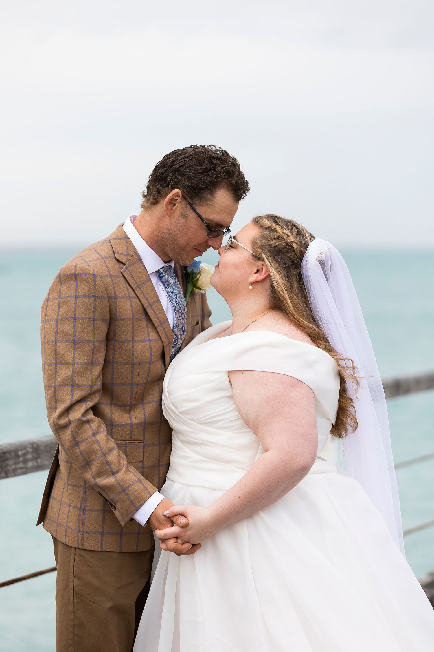 Seaside wedding portraits showing couple in brown suit and white dress against ocean backdrop.