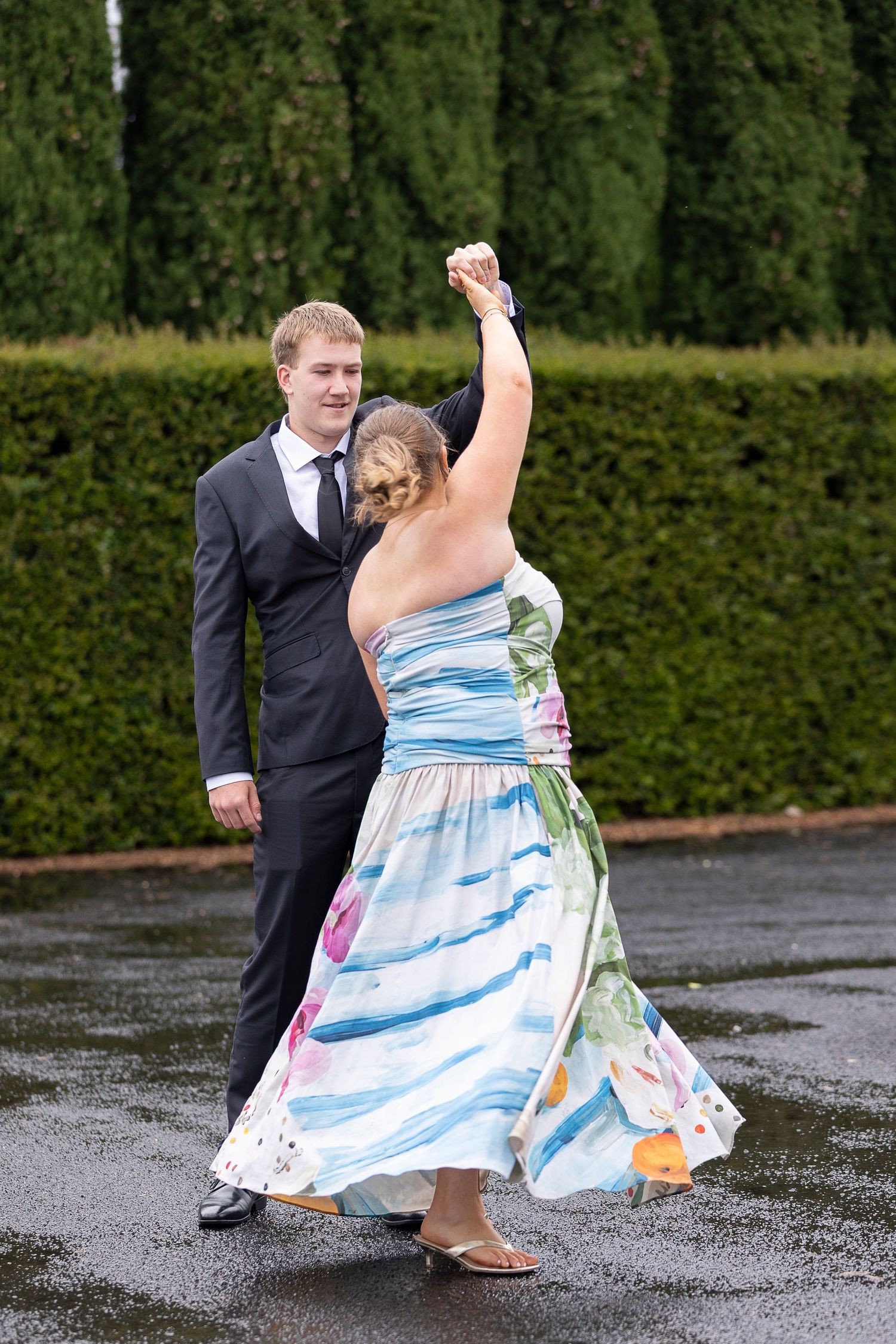 Dancing and celebration captured on wet pavement near green hedges.
