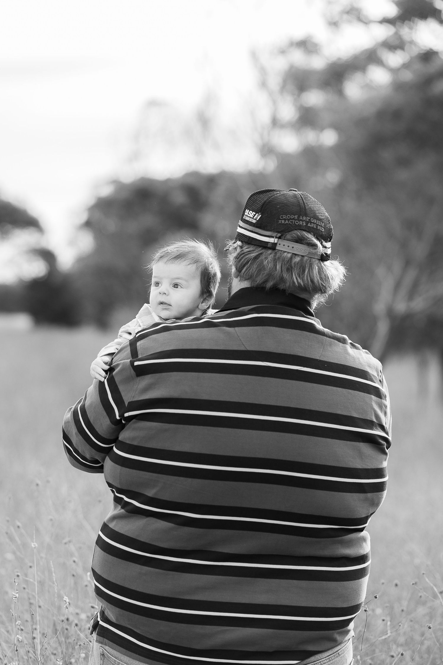 Black and white photo of a person in striped shirt holding a small child in a field.