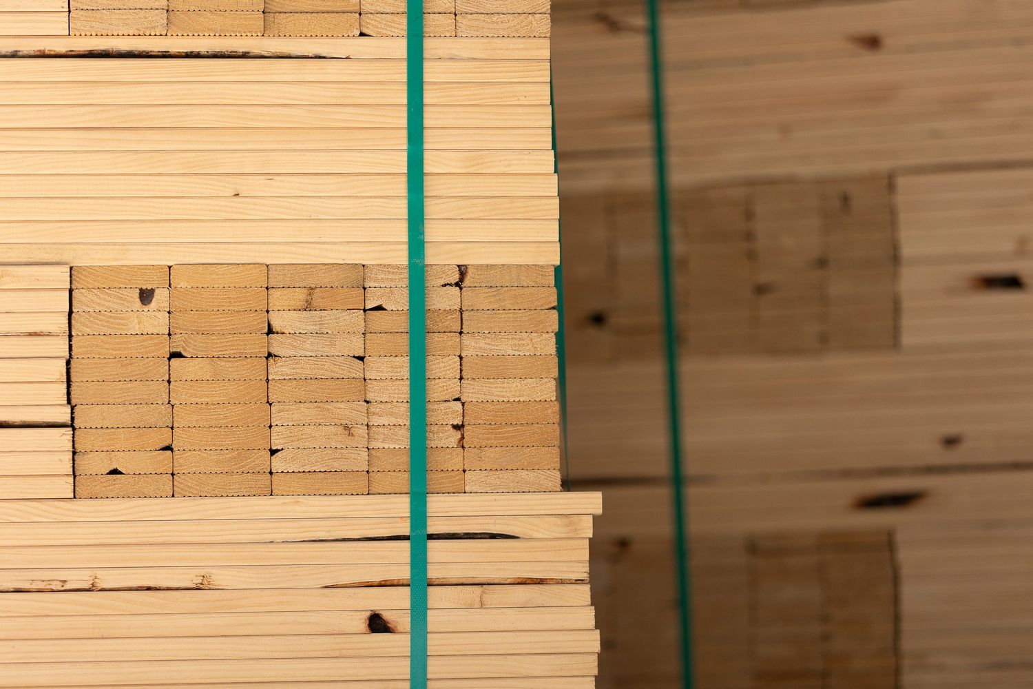 Stacks of light-colored wooden boards with green straps or bands securing them together in a warehouse or lumber yard setting.