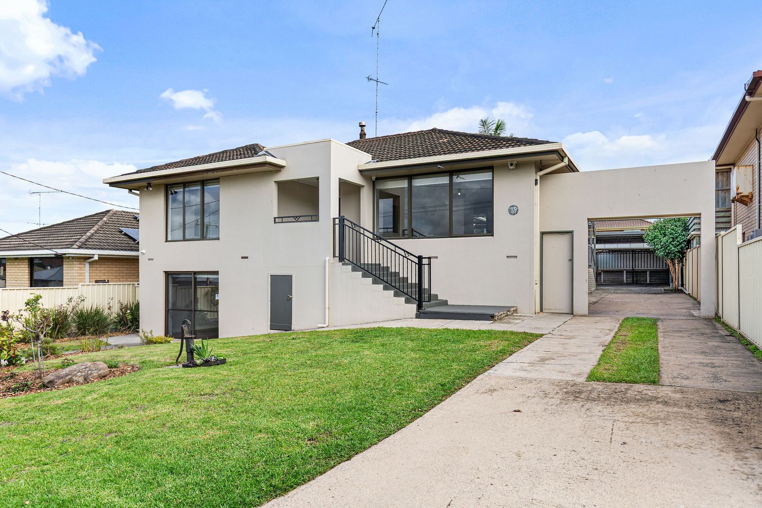 White rendered brick home with balcony, manicured lawn, and double driveway under blue skies in suburban Australia.