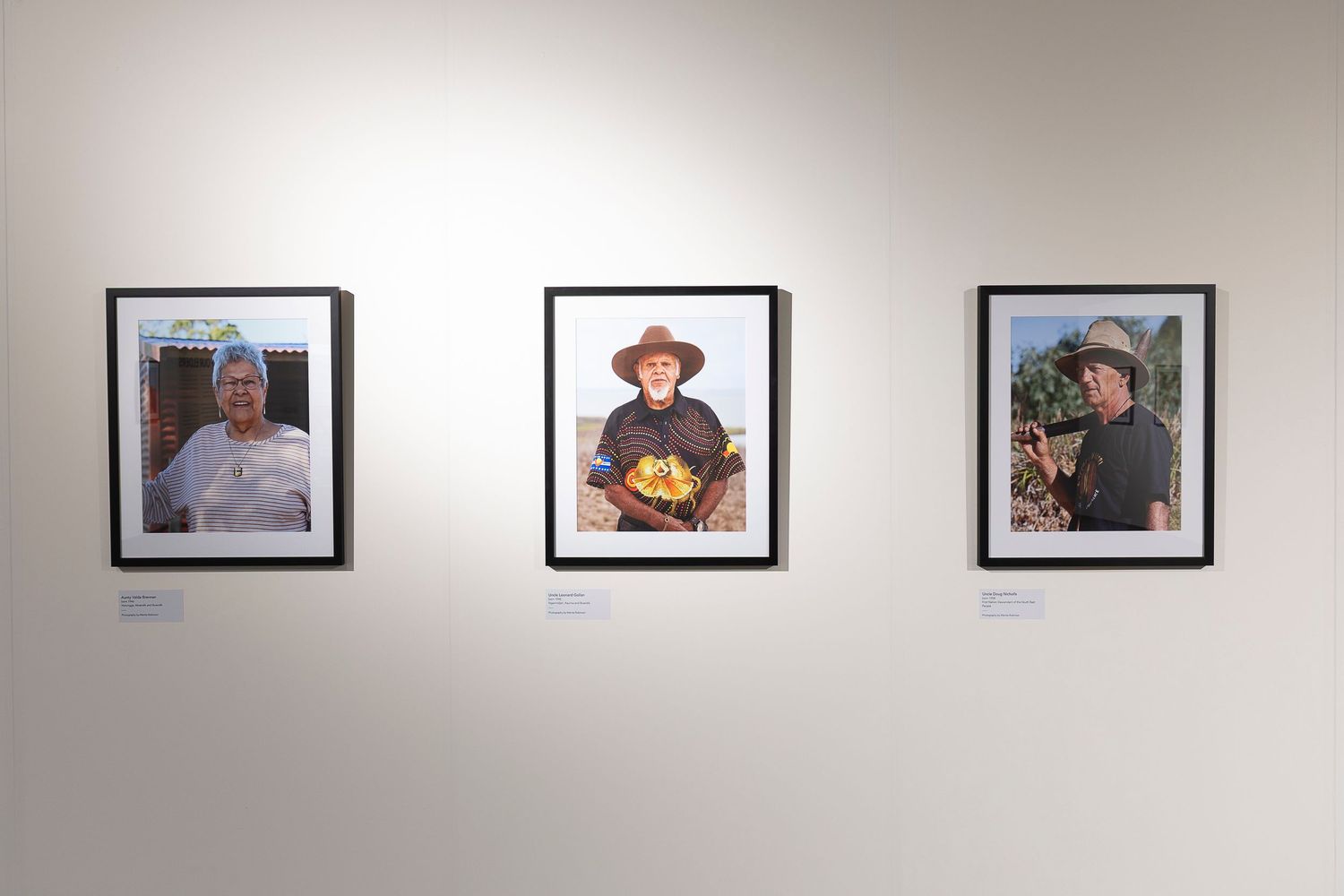 Row of black and white portrait photographs mounted on a white gallery wall.