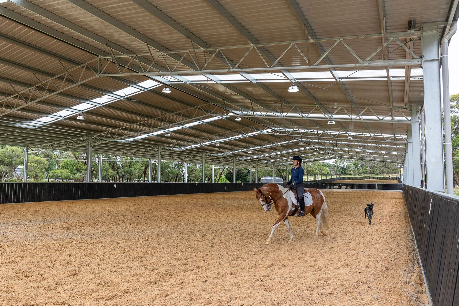 Indoor equestrian arena with riders practicing dressage.