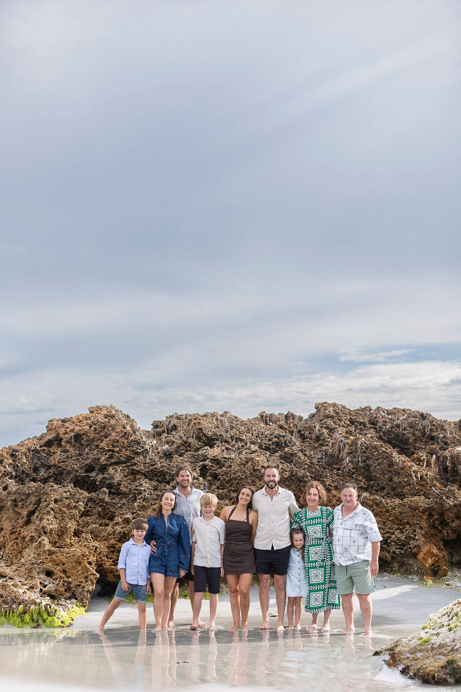 A group poses together on a beach with rocky outcrops and cloudy skies.