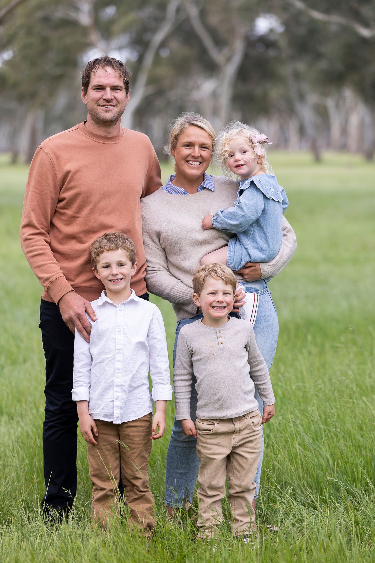 Family group portrait in casual clothing standing together in green field.