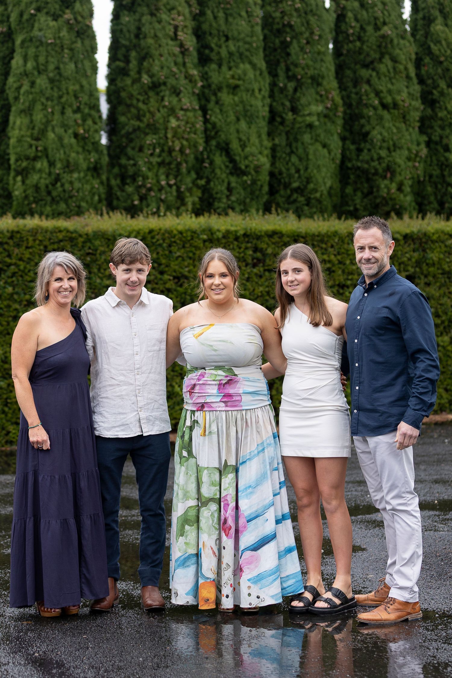 A group poses together against a hedge backdrop on a rainy day.