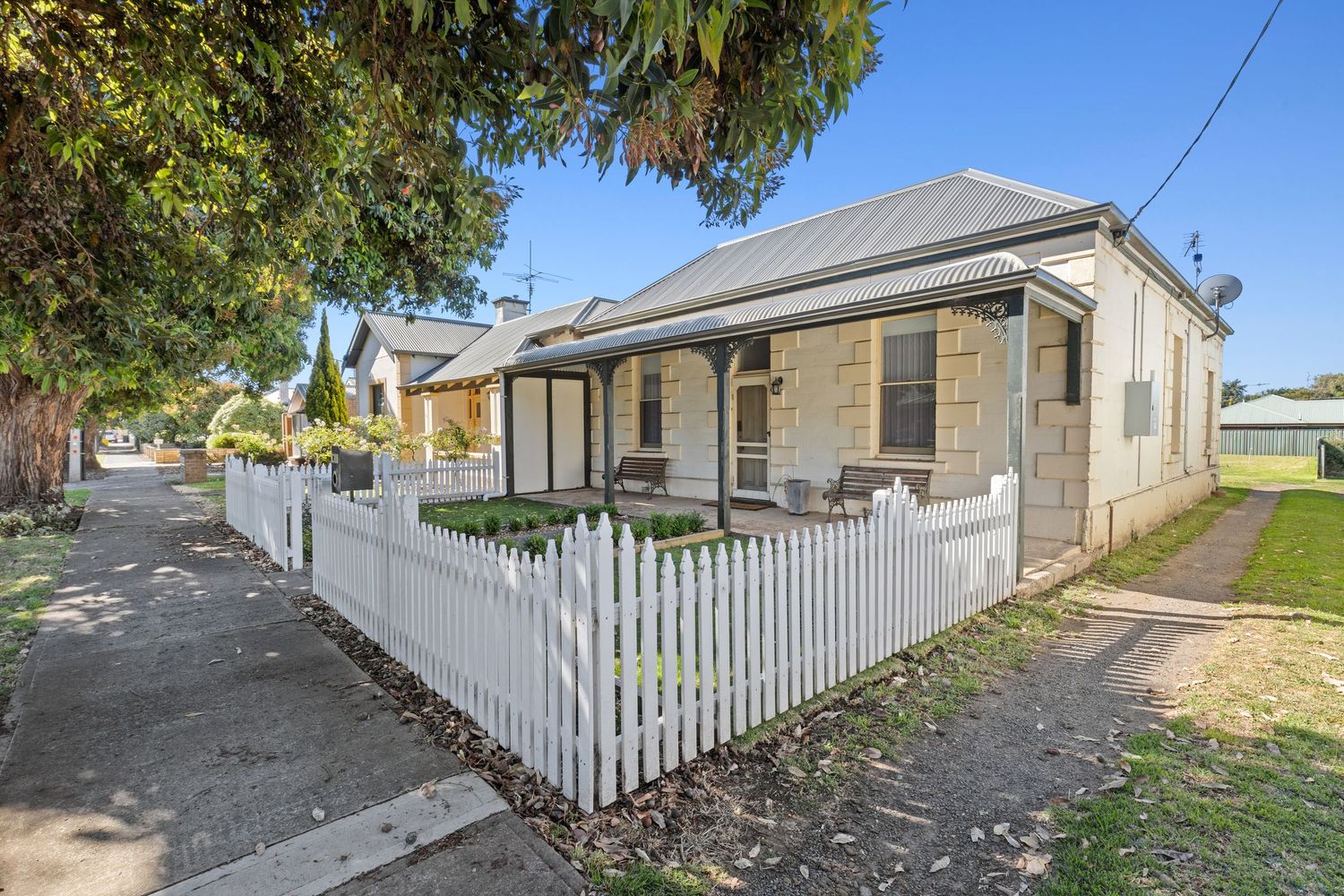 Charming cottage exterior with white picket fence and established trees along a residential street.