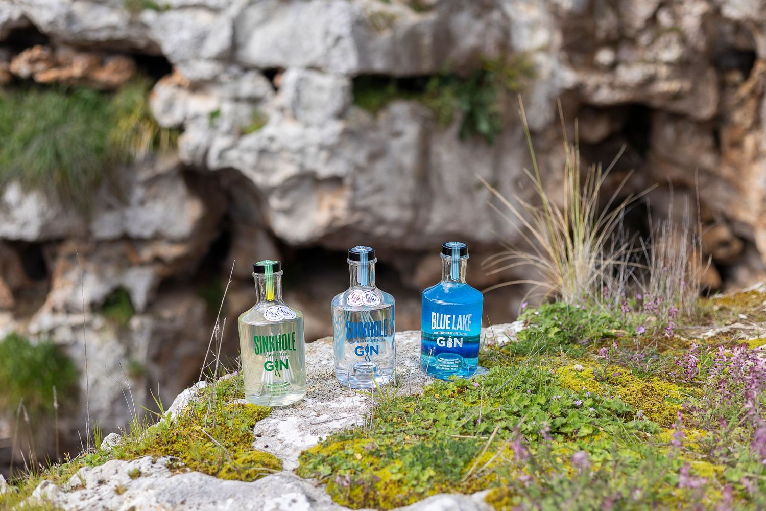 Three blue glass bottles arranged on moss covered rocks near a limestone formation.