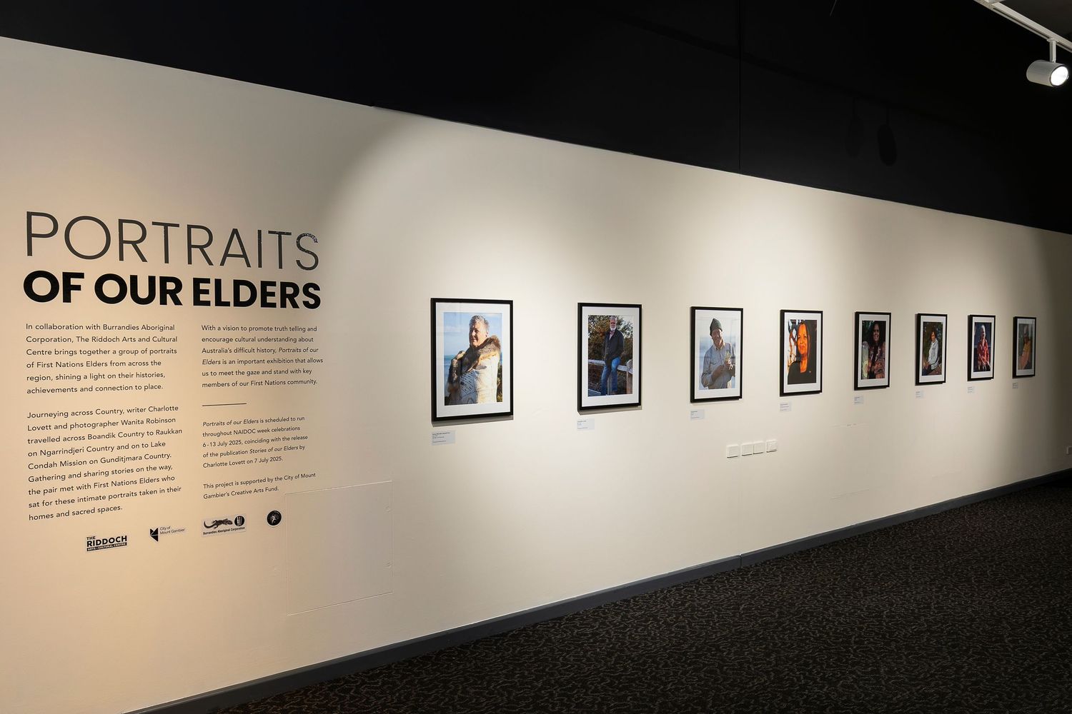 Exhibition space with 'Portraits' text and multiple framed photographs displayed on white walls.