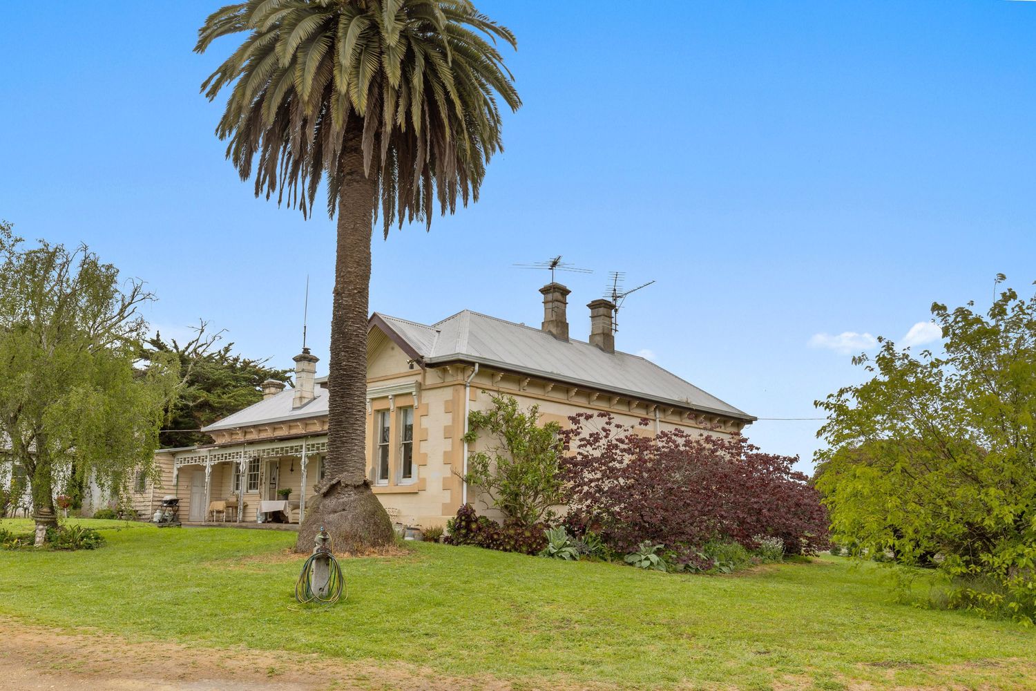 Historic homestead with palm trees and landscaped gardens under blue sky.