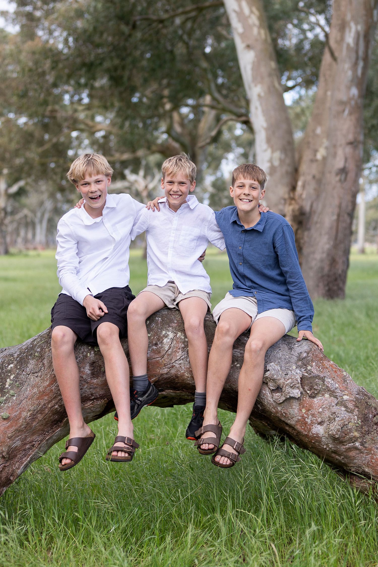 Three young people in casual attire sitting together on a large rock in a park setting.
