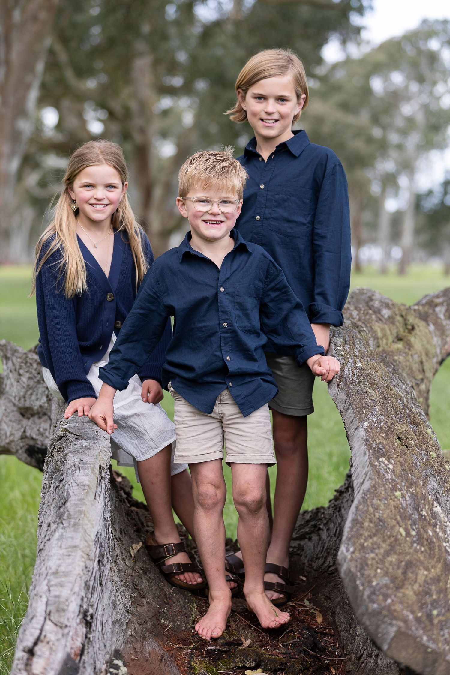 Children sitting together on a fallen tree trunk wearing matching navy outfits.