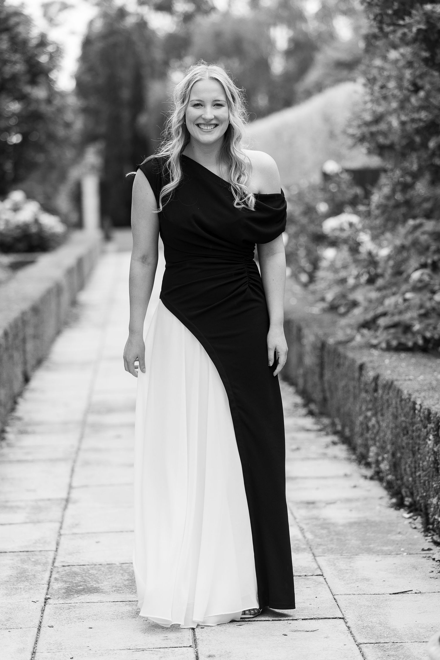 Black and white photos of someone wearing a contrast dress posing along a garden pathway.