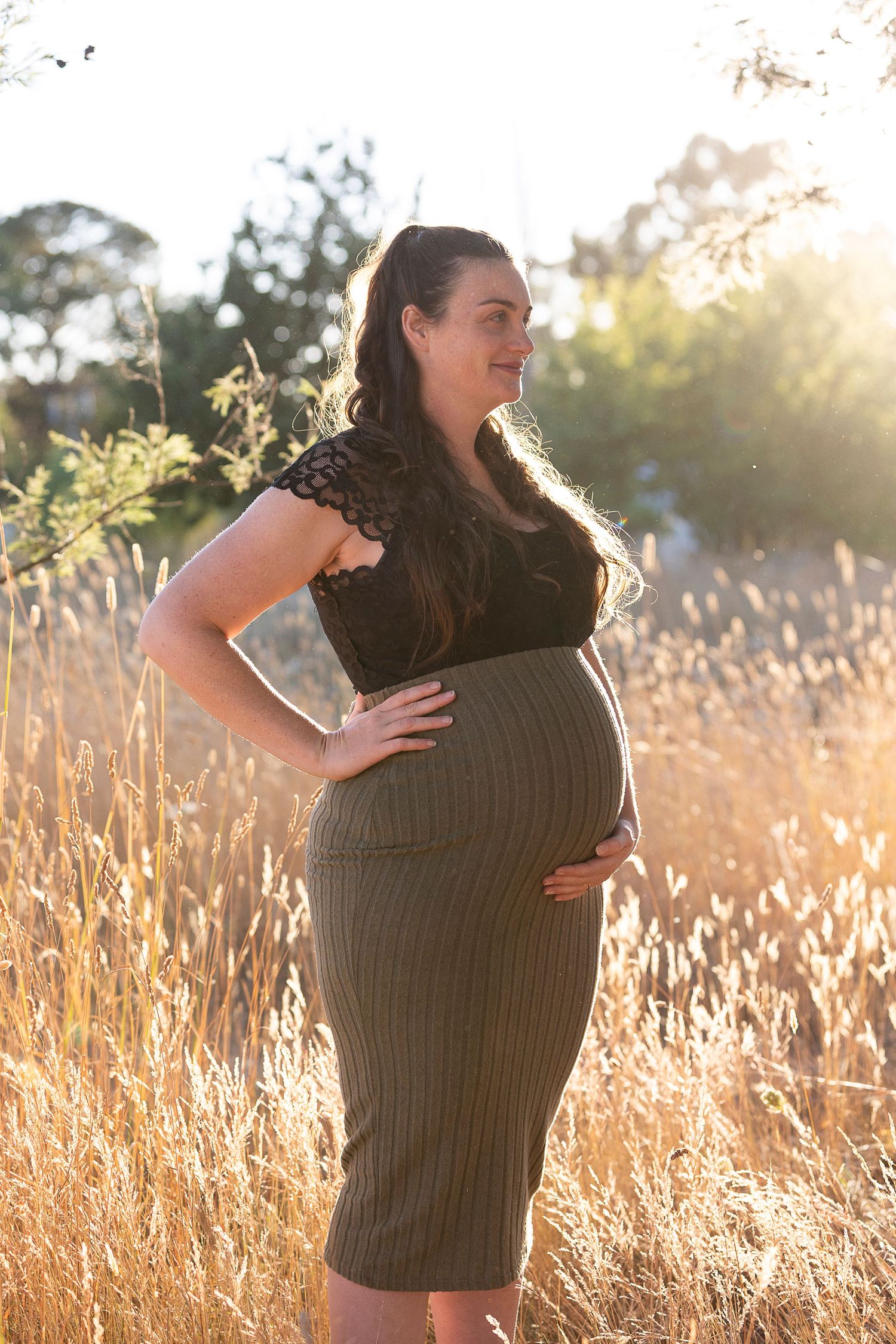 Woman in dark dress standing in sunlit field during golden hour.