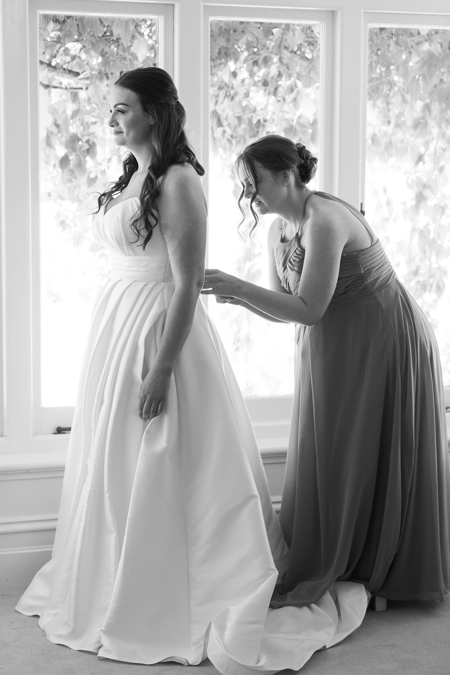 Black and white photo of wedding dress preparations in sunlit room.