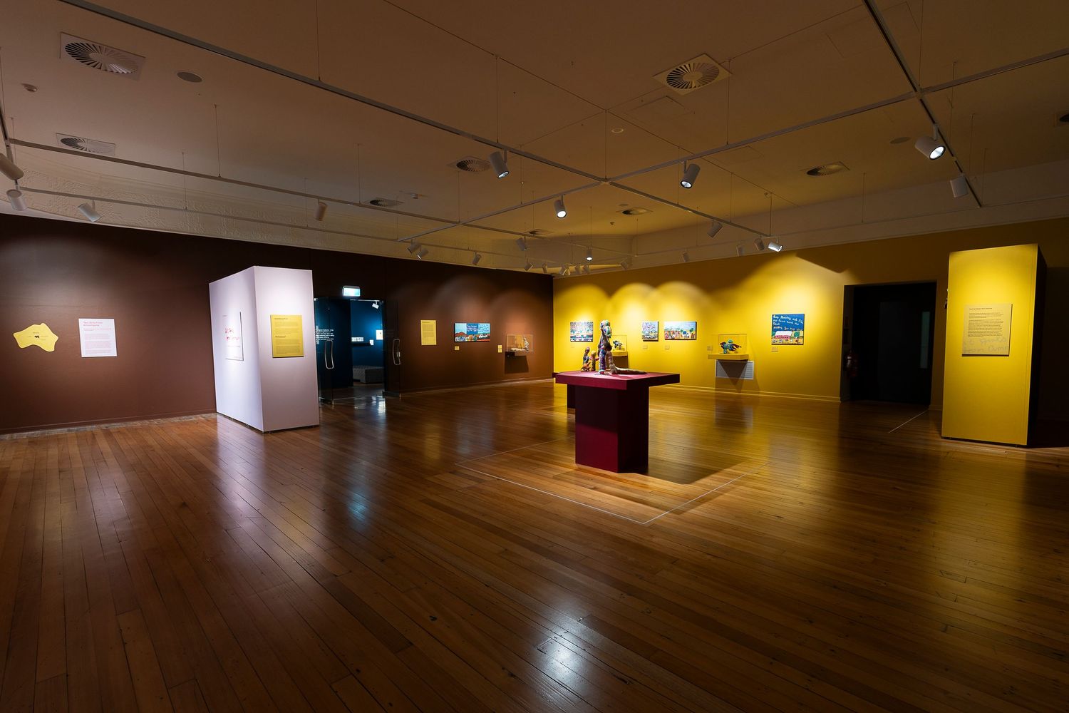 Wide angle view of a contemporary art gallery space with hardwood floors and spotlit displays.