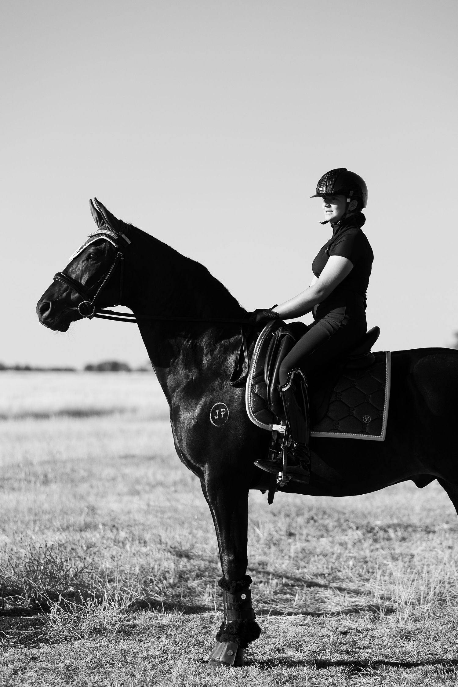 Black and white artistic photo of horse and rider in silhouette against an open field.