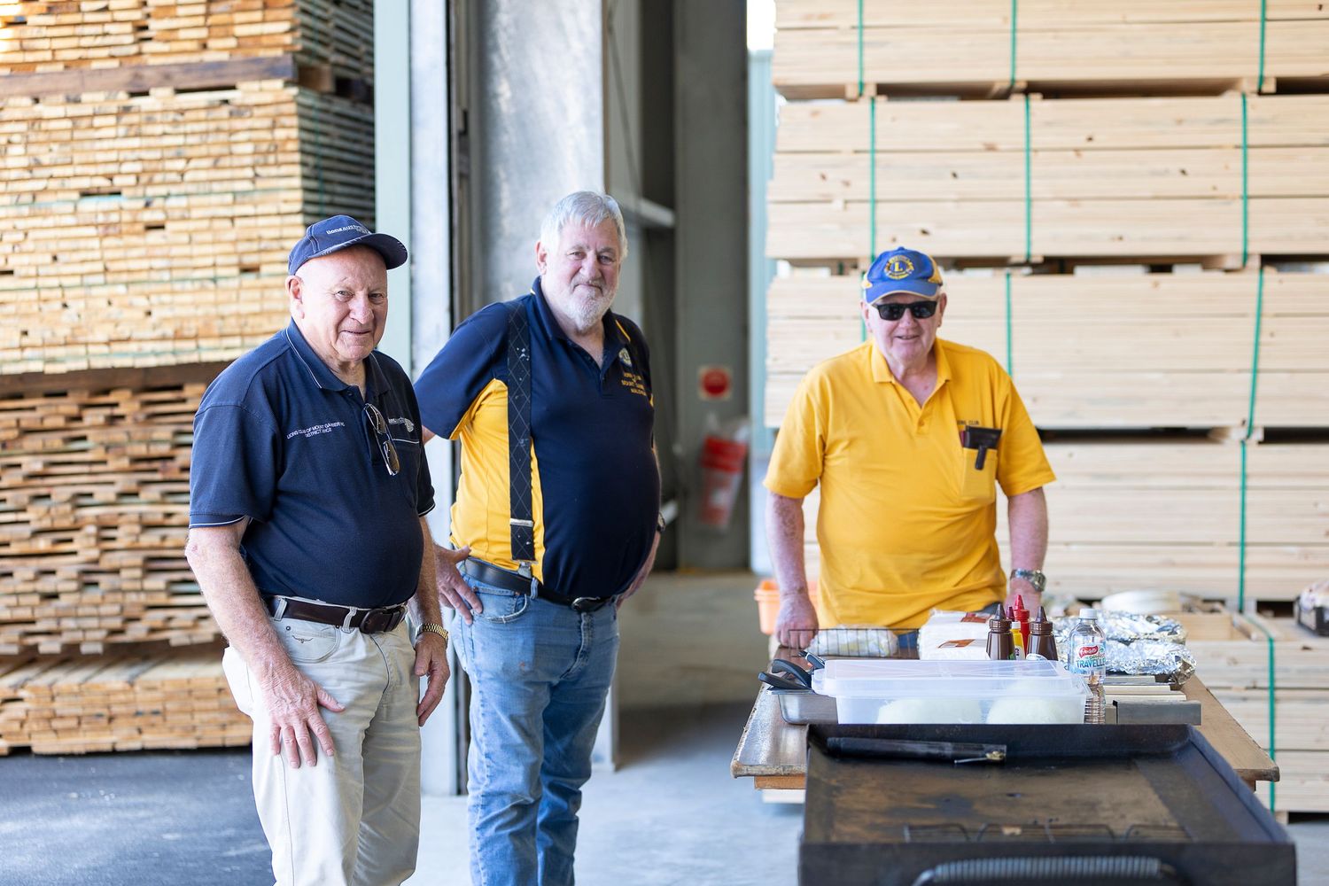 People inspecting stacks of lumber and wooden materials in an industrial warehouse setting.