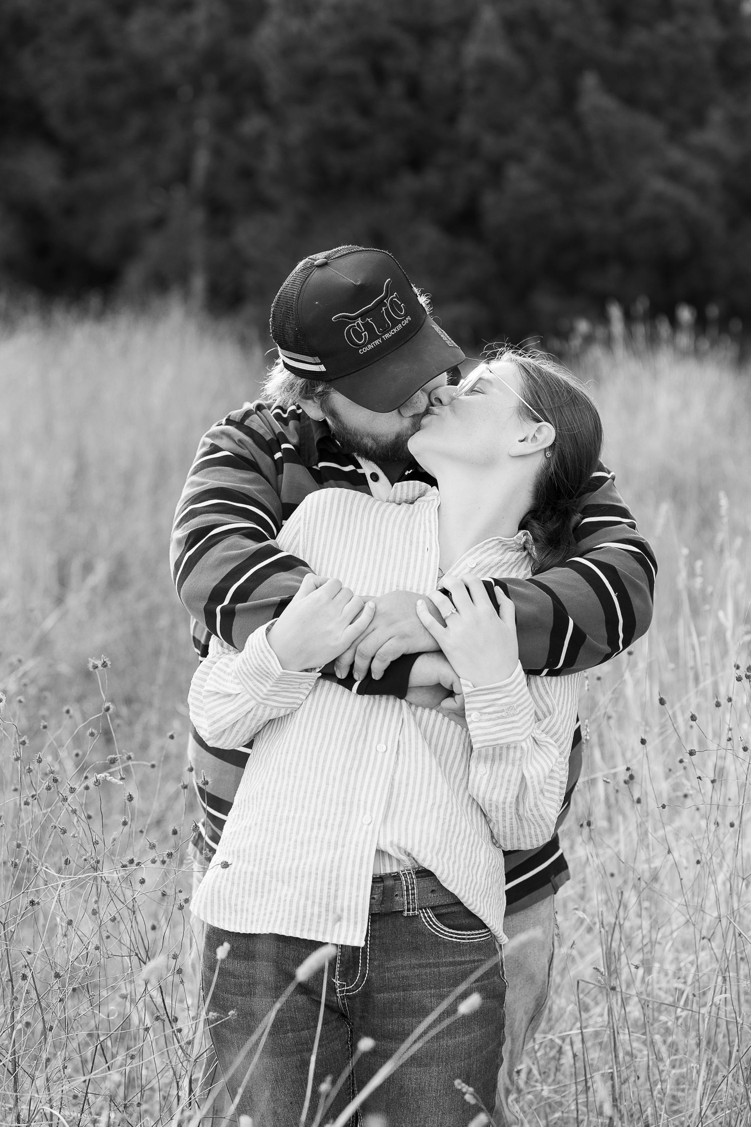 Black and white portrait of couple's tender embrace in field.