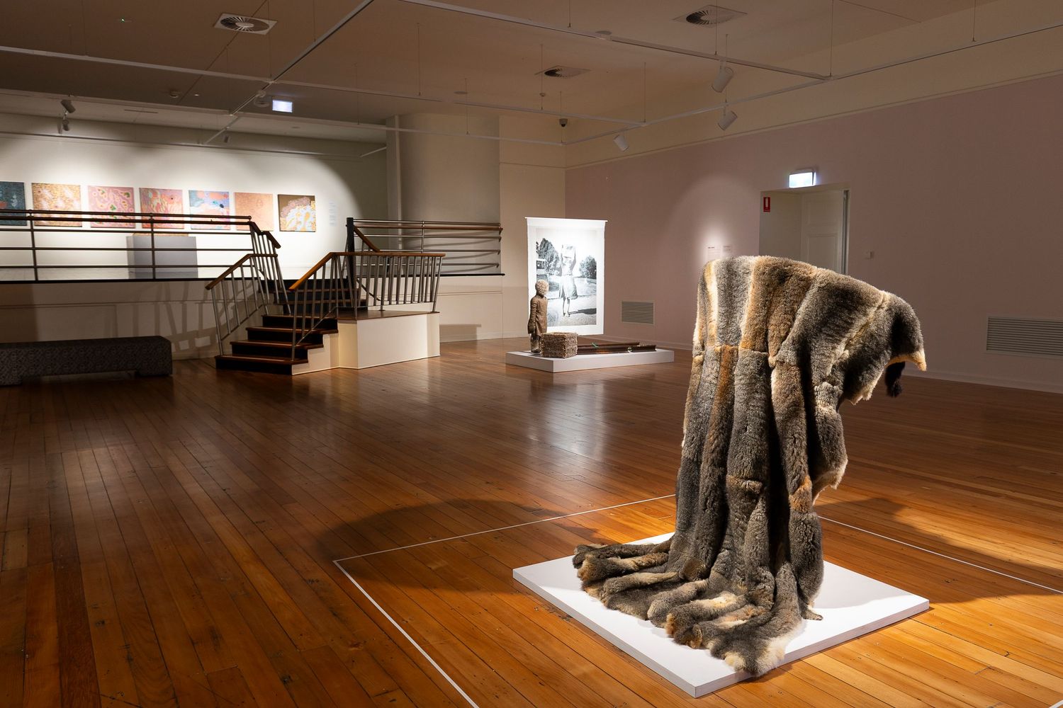 Gallery exhibition space featuring wooden flooring and pedestals for artwork display.