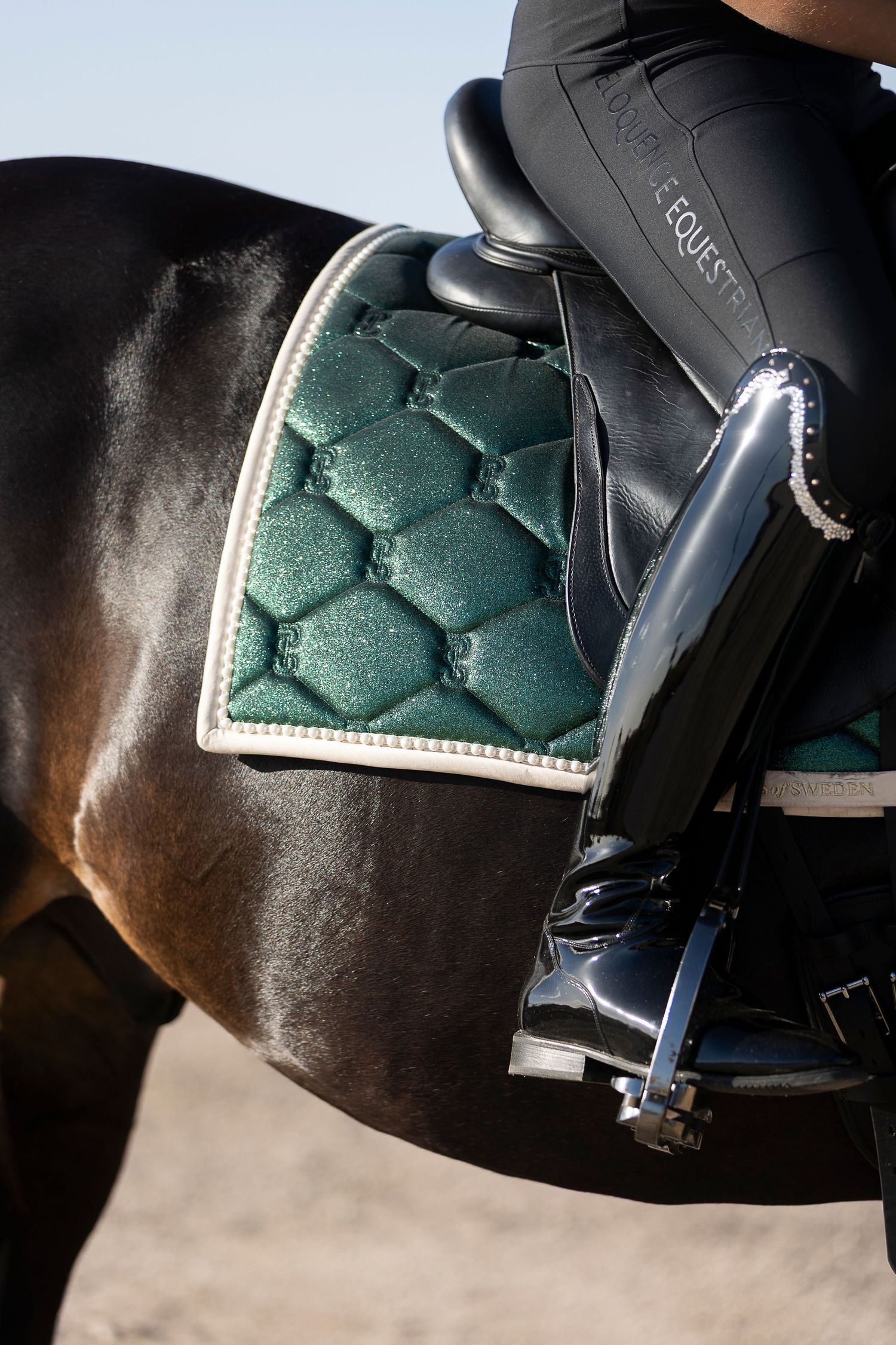 Close-up detail of a green quilted saddle pad on a dark horse.