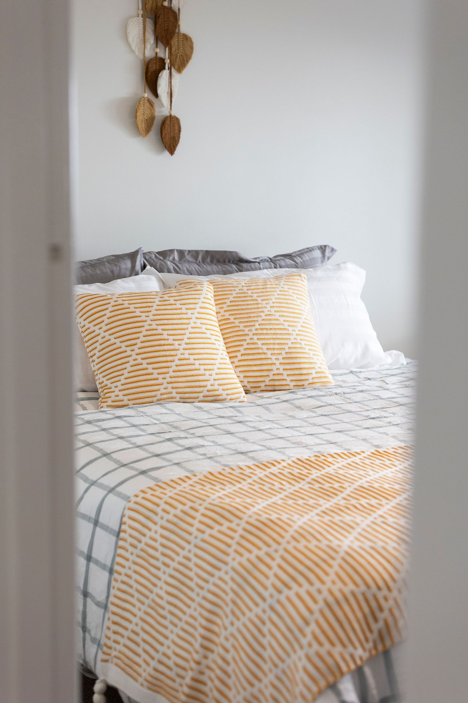 Cozy bedroom with yellow patterned throw blanket and matching pillows on a grey checkered bed with white walls.