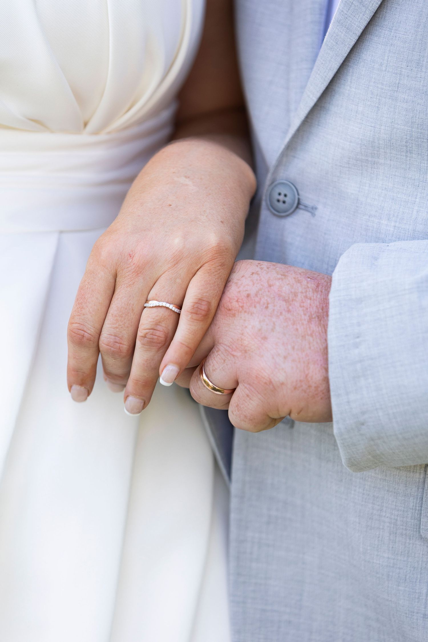 Detail shots of couple's hands and wedding rings against light colored formal attire.