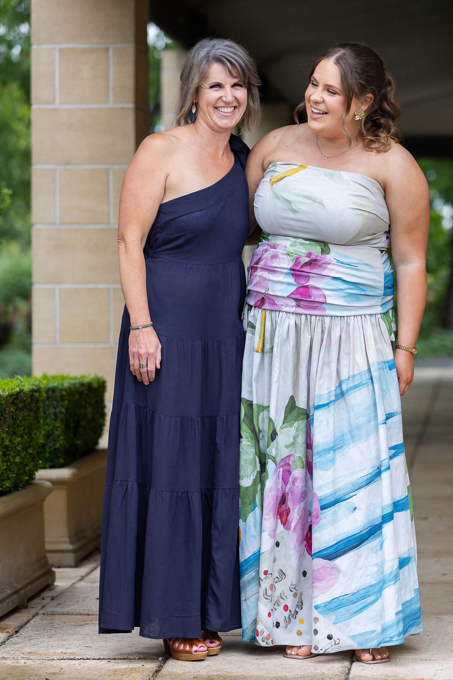Friends posing together in navy and floral dresses against stone backdrop.