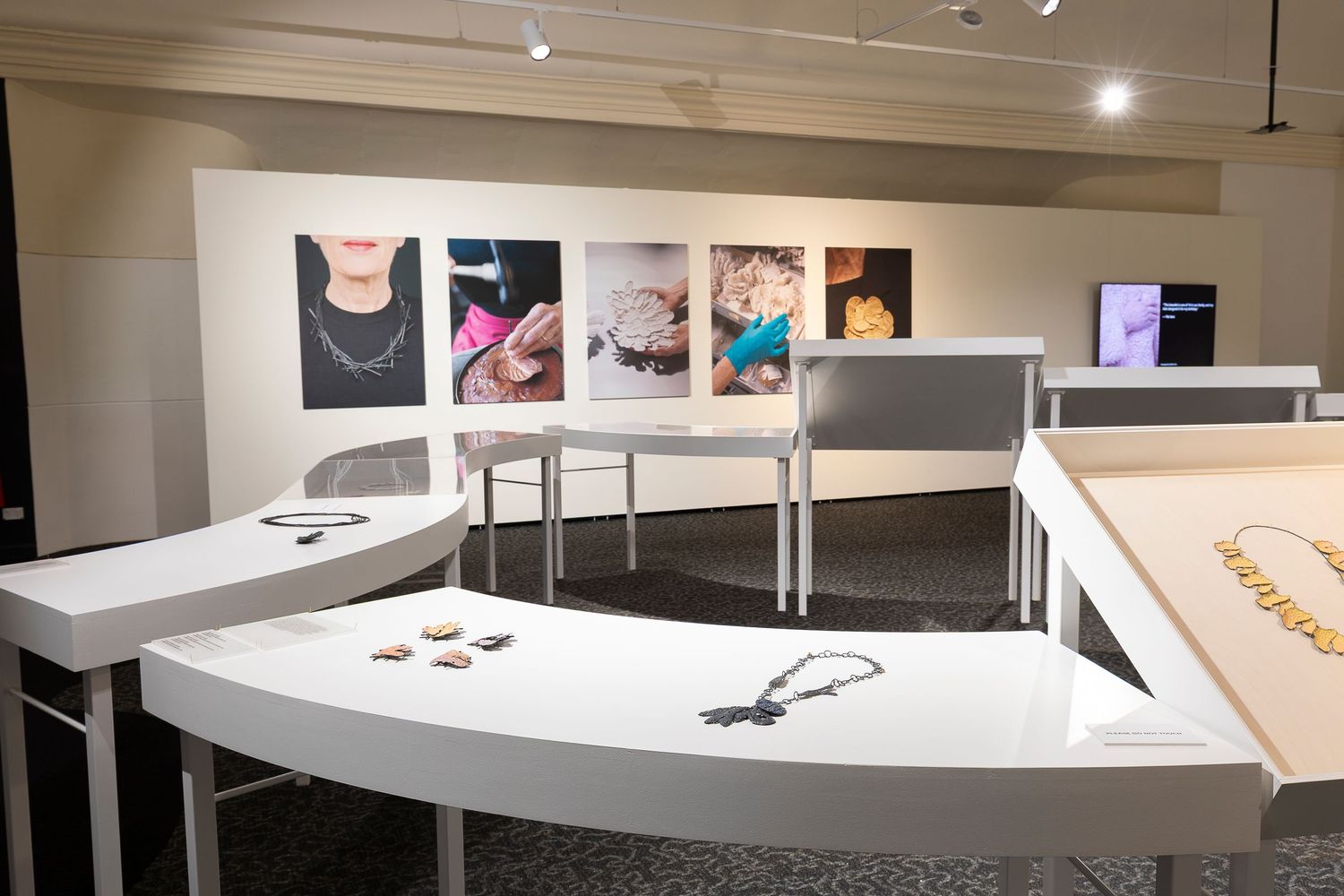 Panoramic view of an art gallery showing curved display tables and wall-mounted artwork.