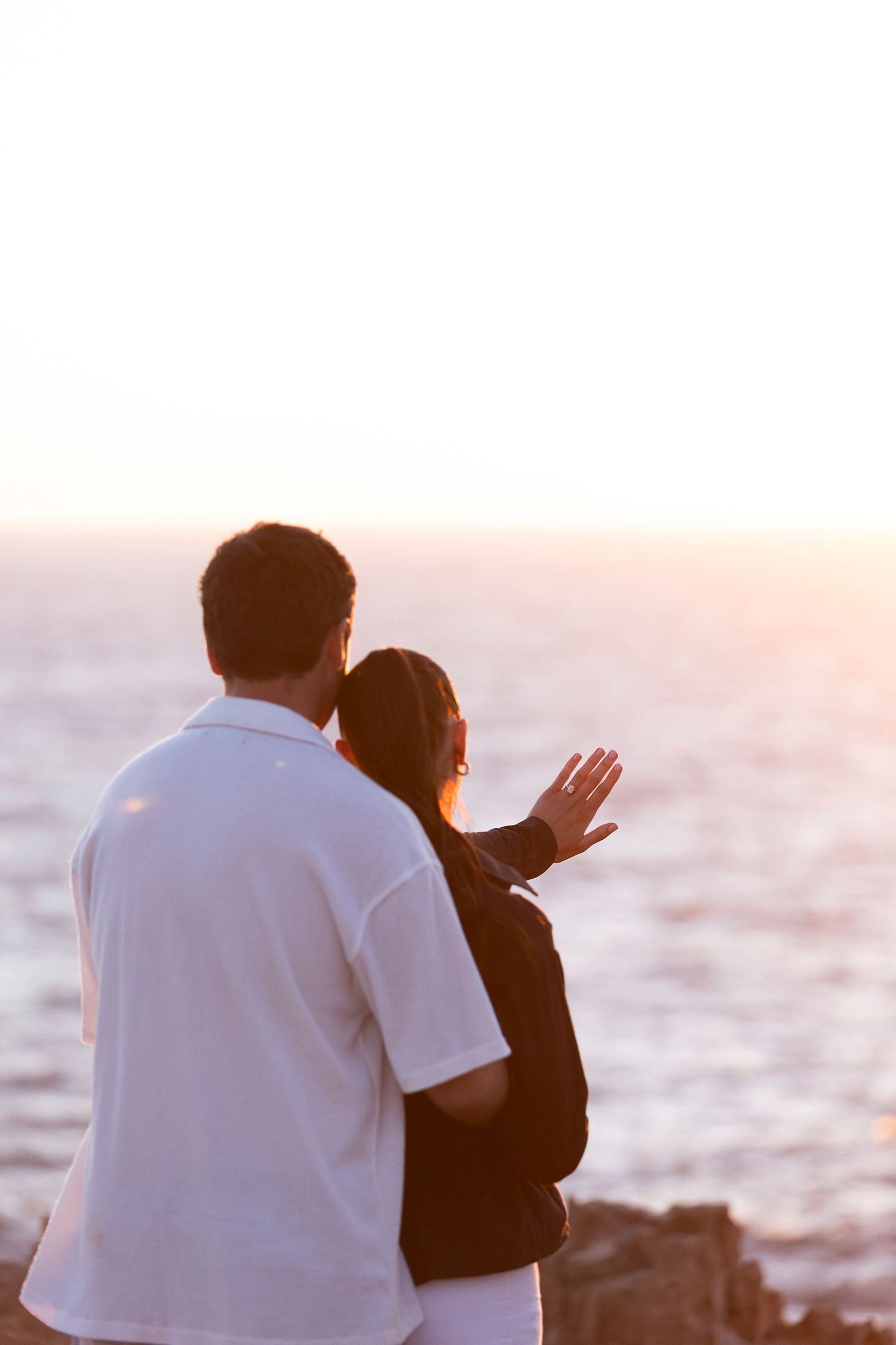 A couple shares a tender moment by the ocean during sunset.