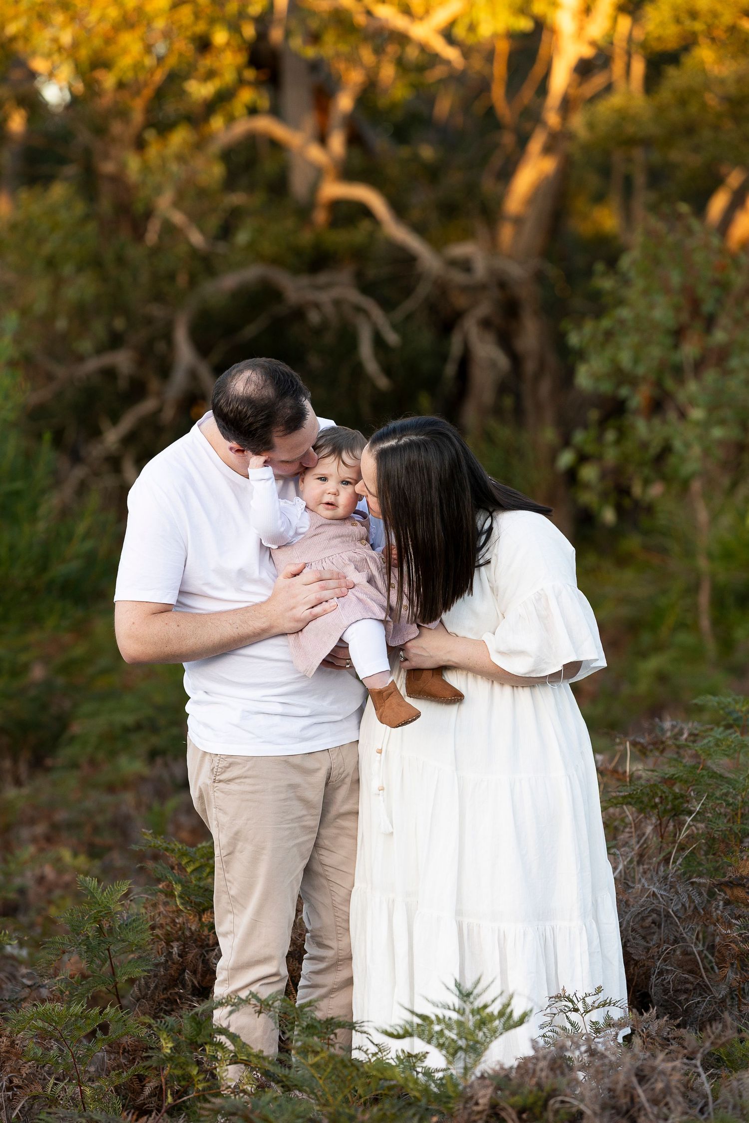 Intimate family moment captured in front of autumn trees at sunset.