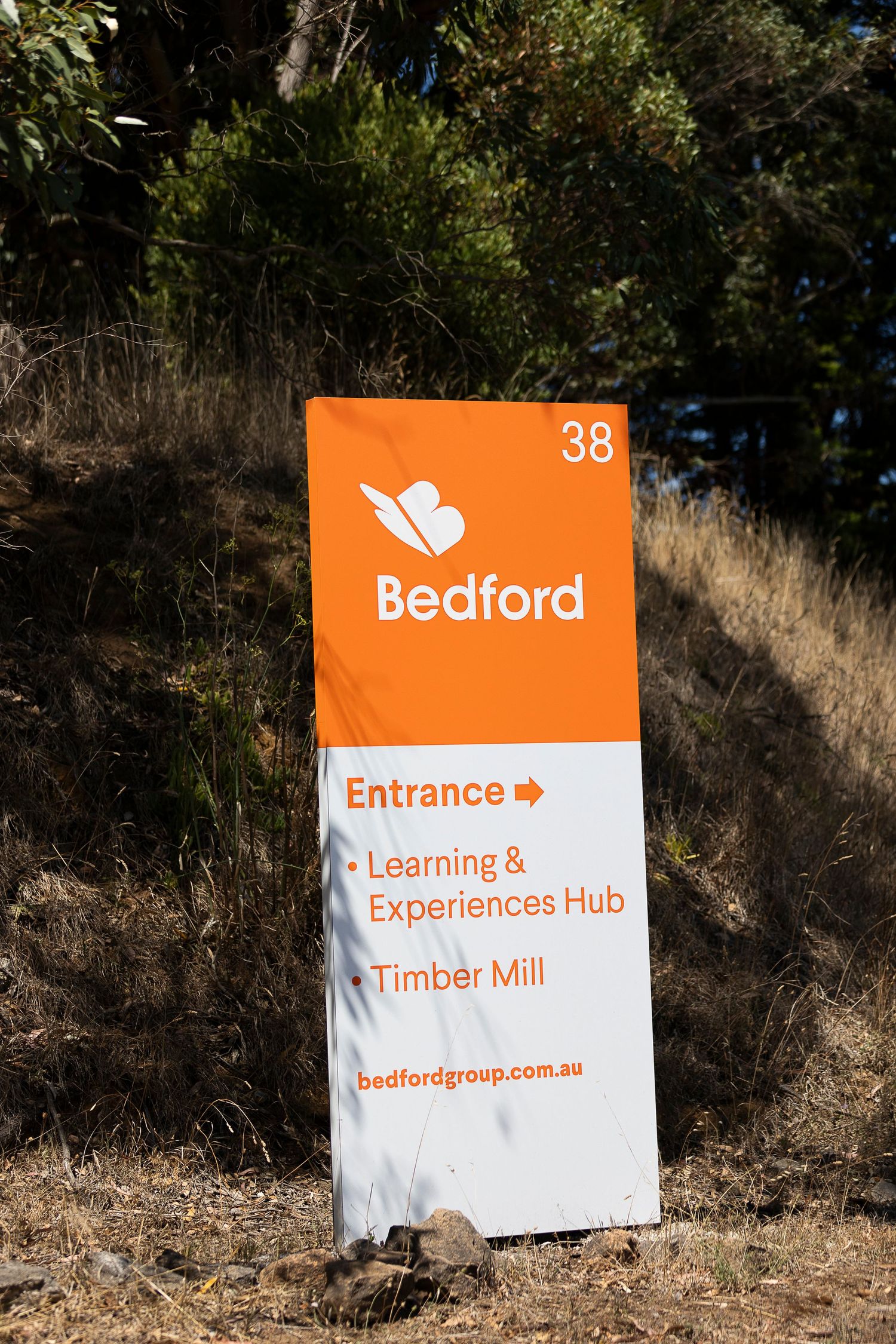 Orange directional sign for Bedford facility entrance pointing to Learning Hub and Timber Mill.