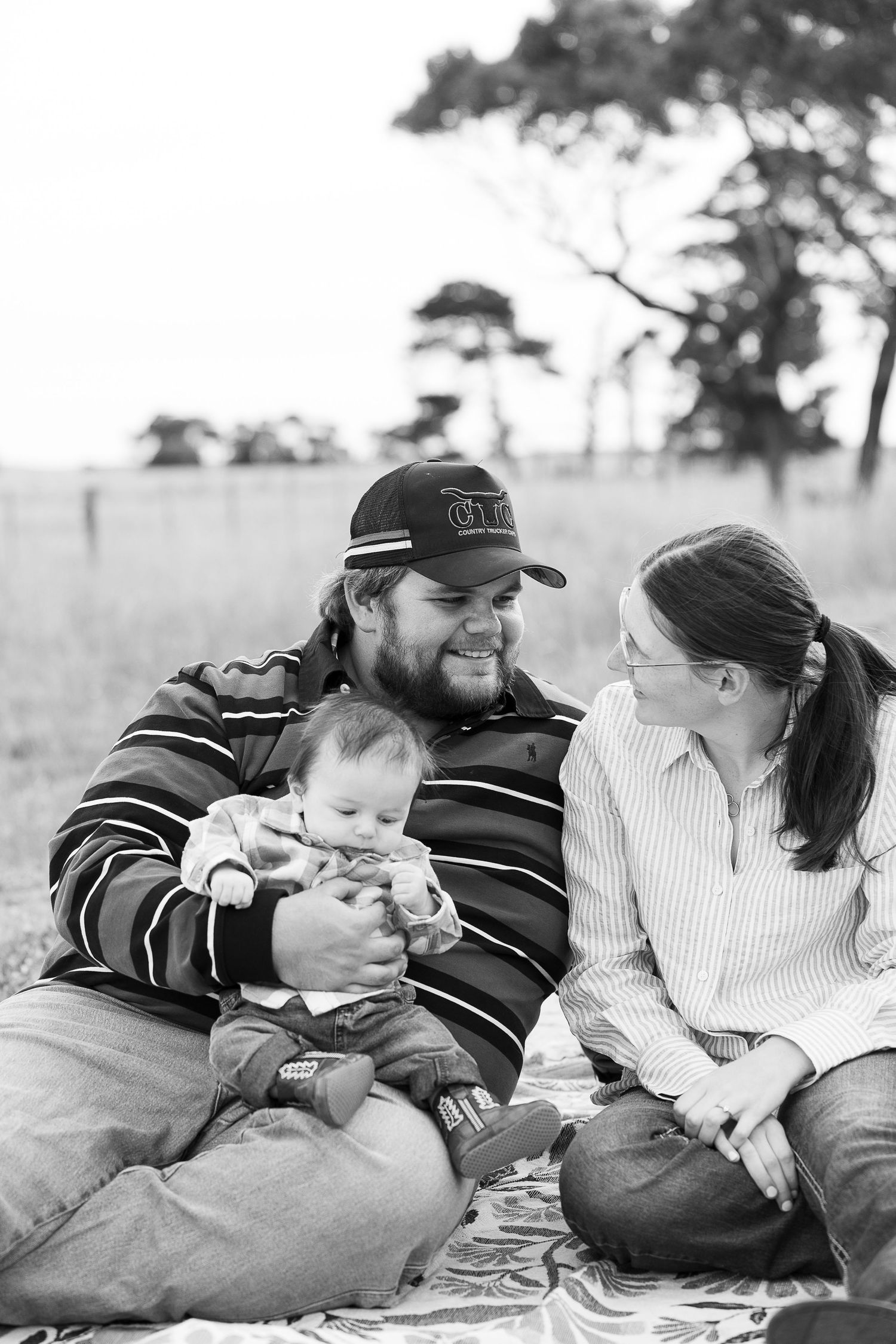 Family laying together on a blanket outdoors sharing an intimate moment.