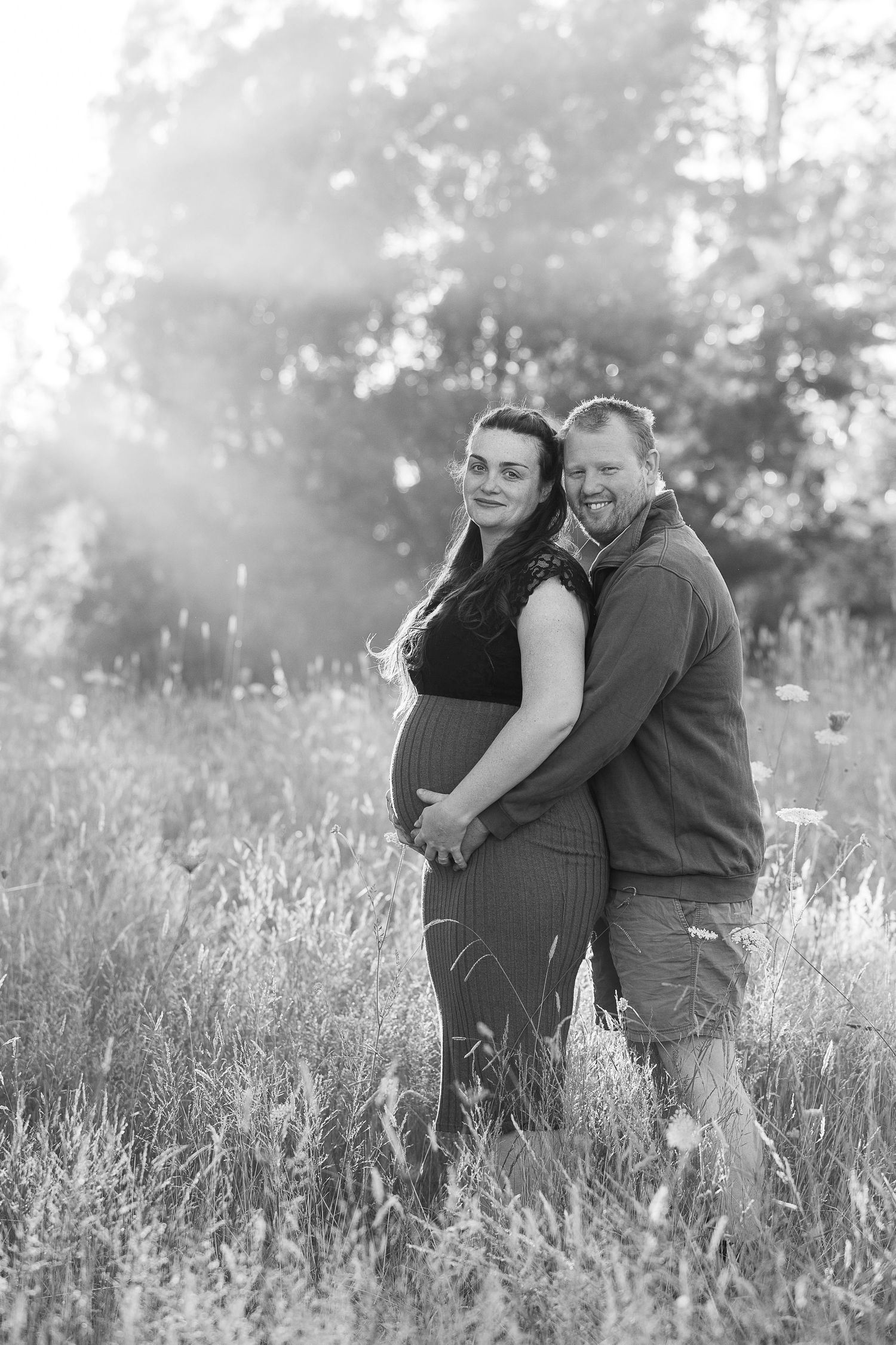Expecting couple shares a joyful moment together in a sunlit meadow.