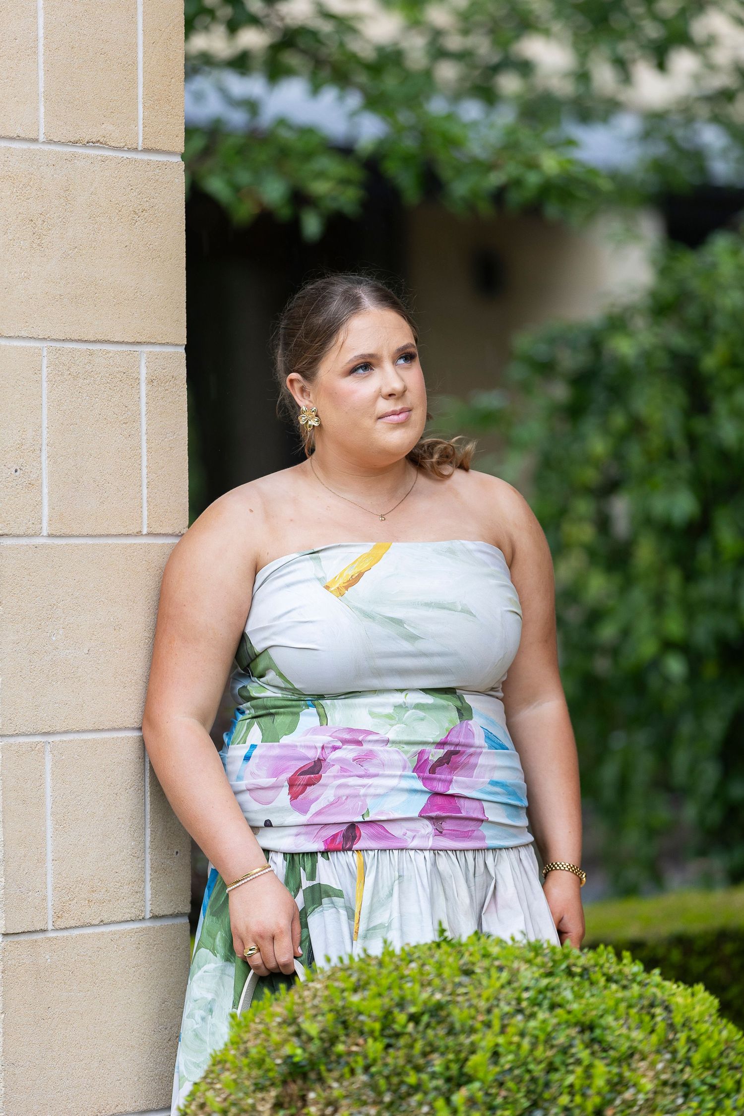 Strapless floral dress photographed against brick wall and garden backdrop.