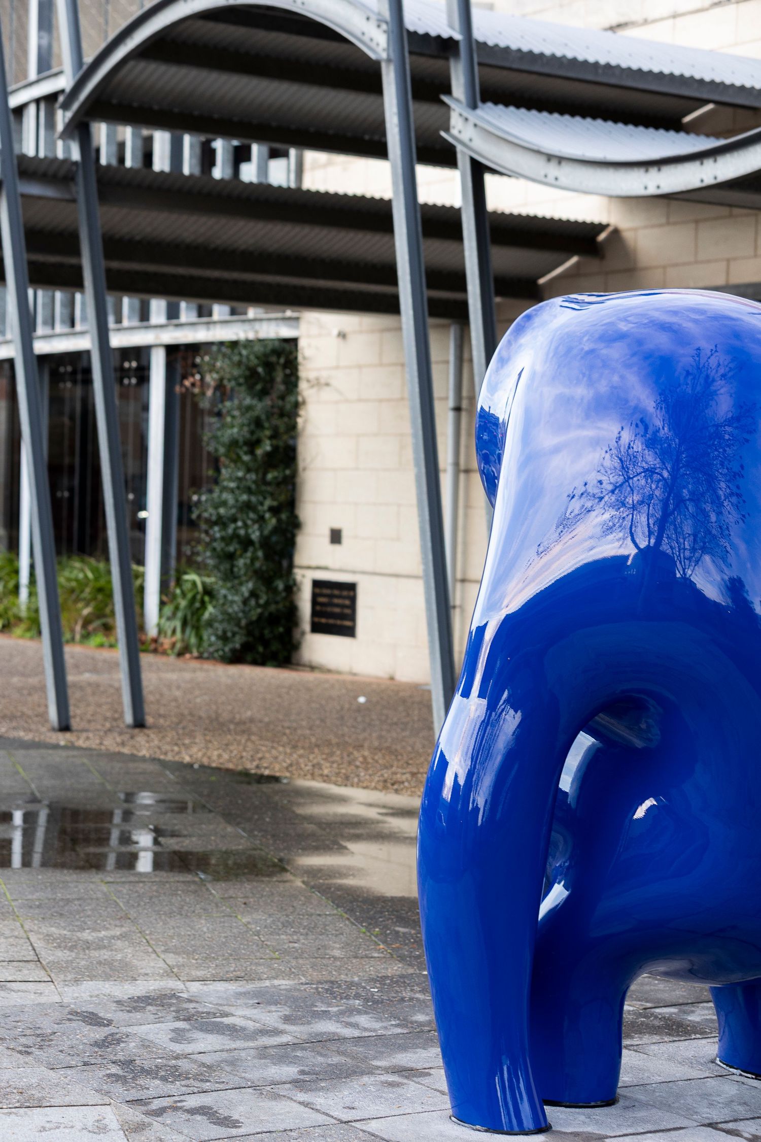 Blue sculpture installation viewed under covered walkway.