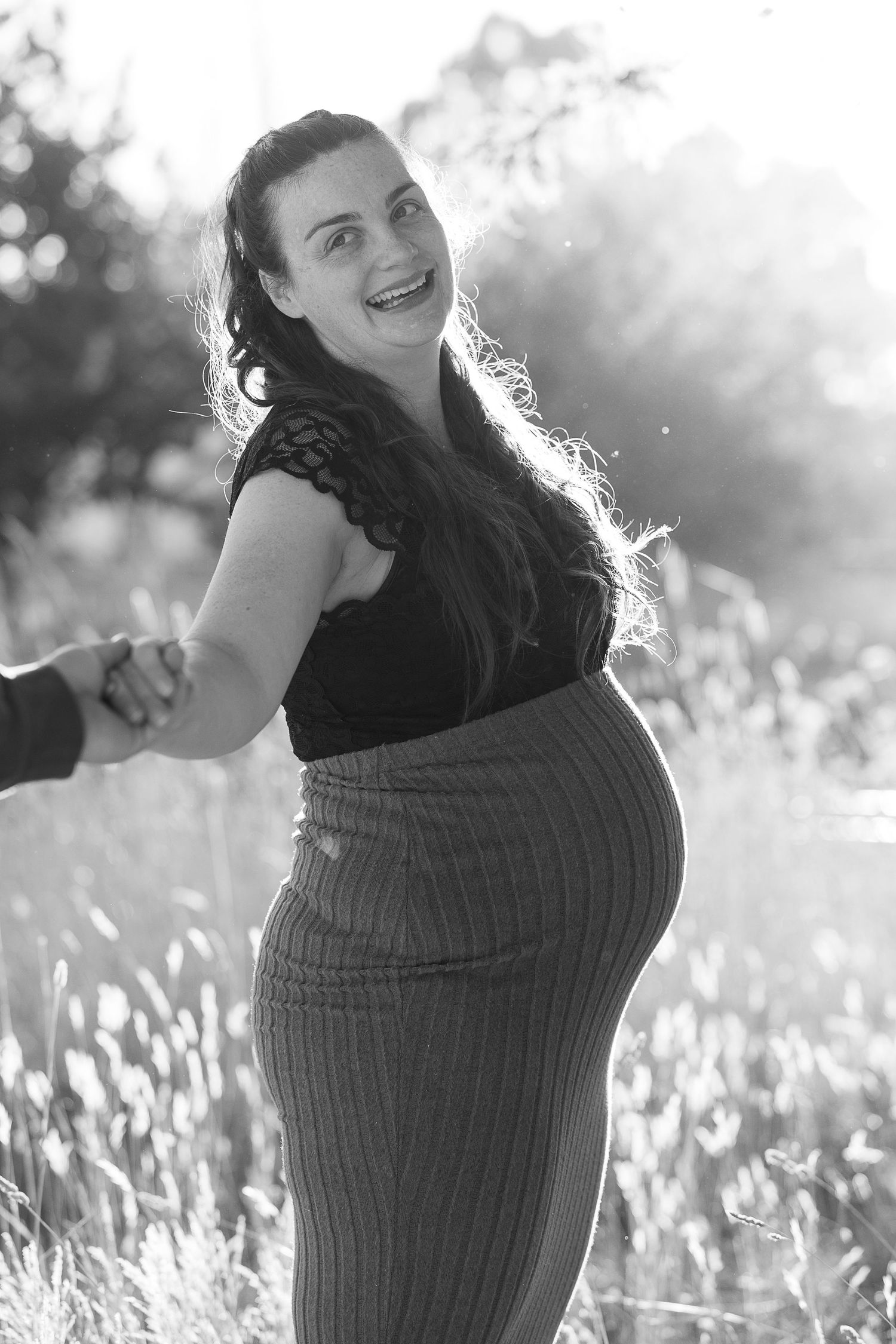 Woman smiling and laughing in a field backlit by golden sunlight.