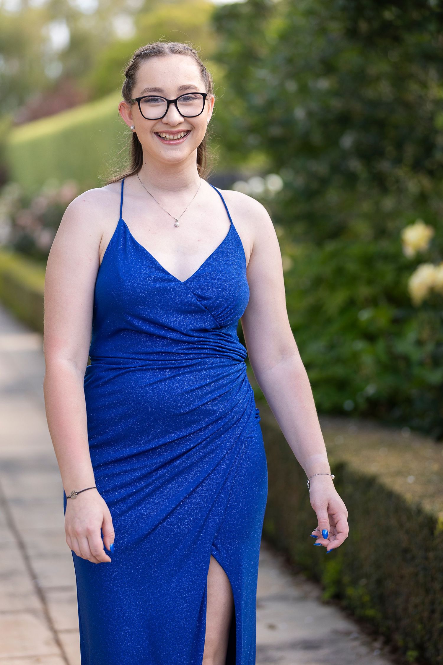 A person in a royal blue formal dress poses in front of manicured hedges.