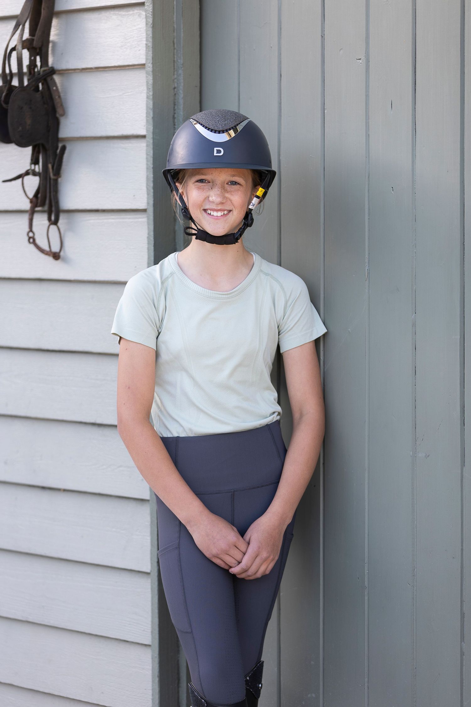 Equestrian wearing riding gear posing against a gray wall.