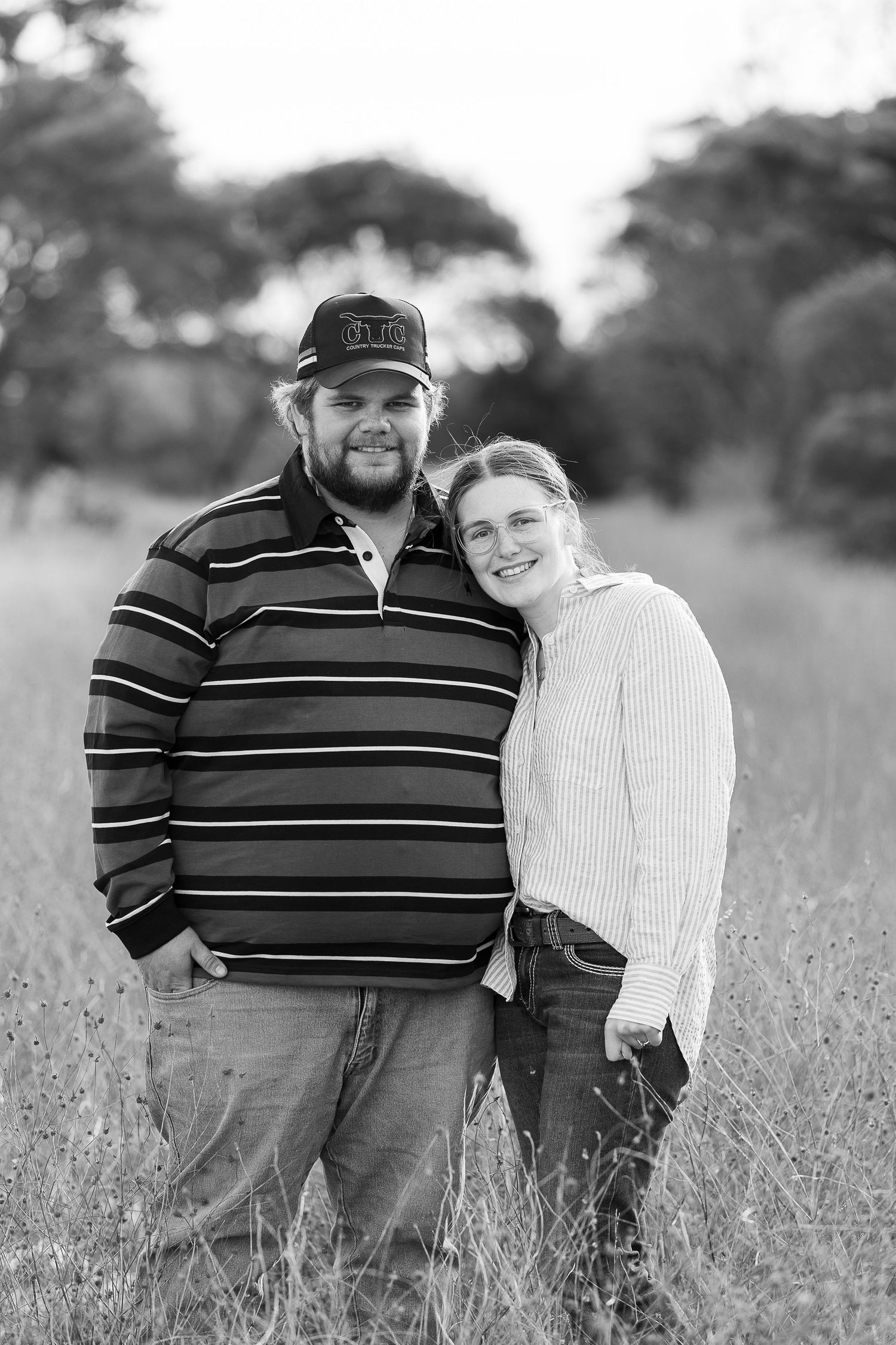 A couple poses together in a field of tall grass in black and white.