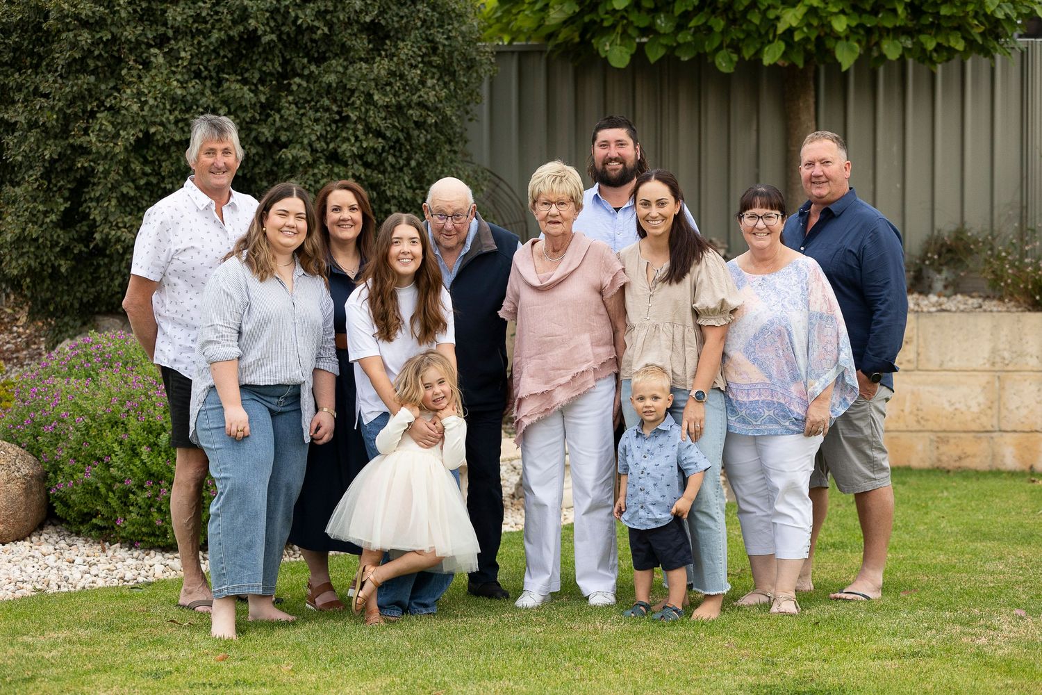 Extended family group poses together on grass against a garden backdrop.
