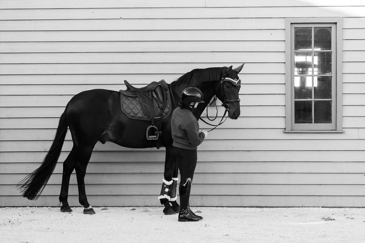 Black and white panoramic view of horses and riders along a building wall.