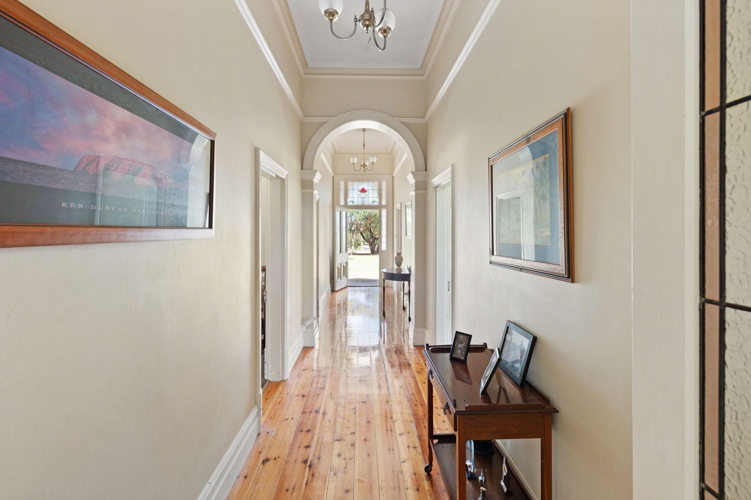 Elegant hallway with polished hardwood floors, arched doorway, chandelier, and artwork in a classic Australian home.