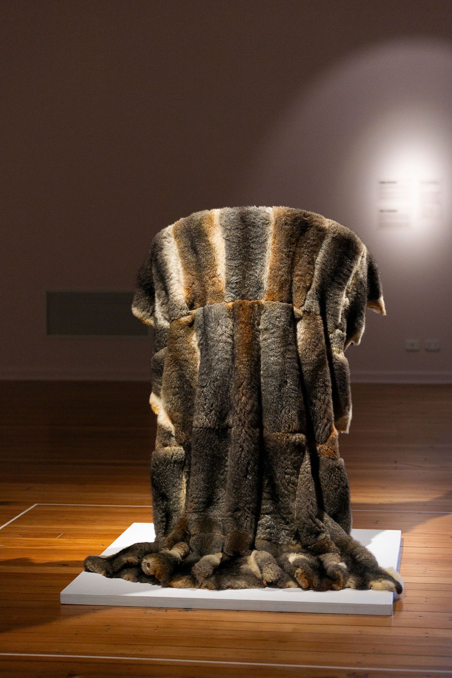 Textured fur artwork installation displayed on white pedestal in museum gallery space.