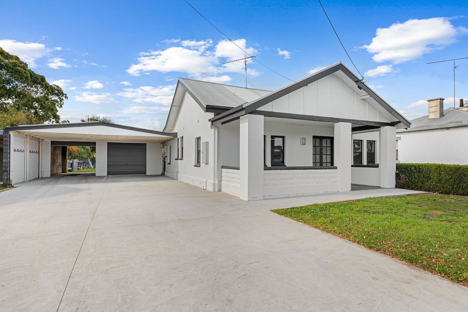 Renovated white weatherboard home with double garage, wide concrete driveway, covered porch, and manicured lawn under blue sky.