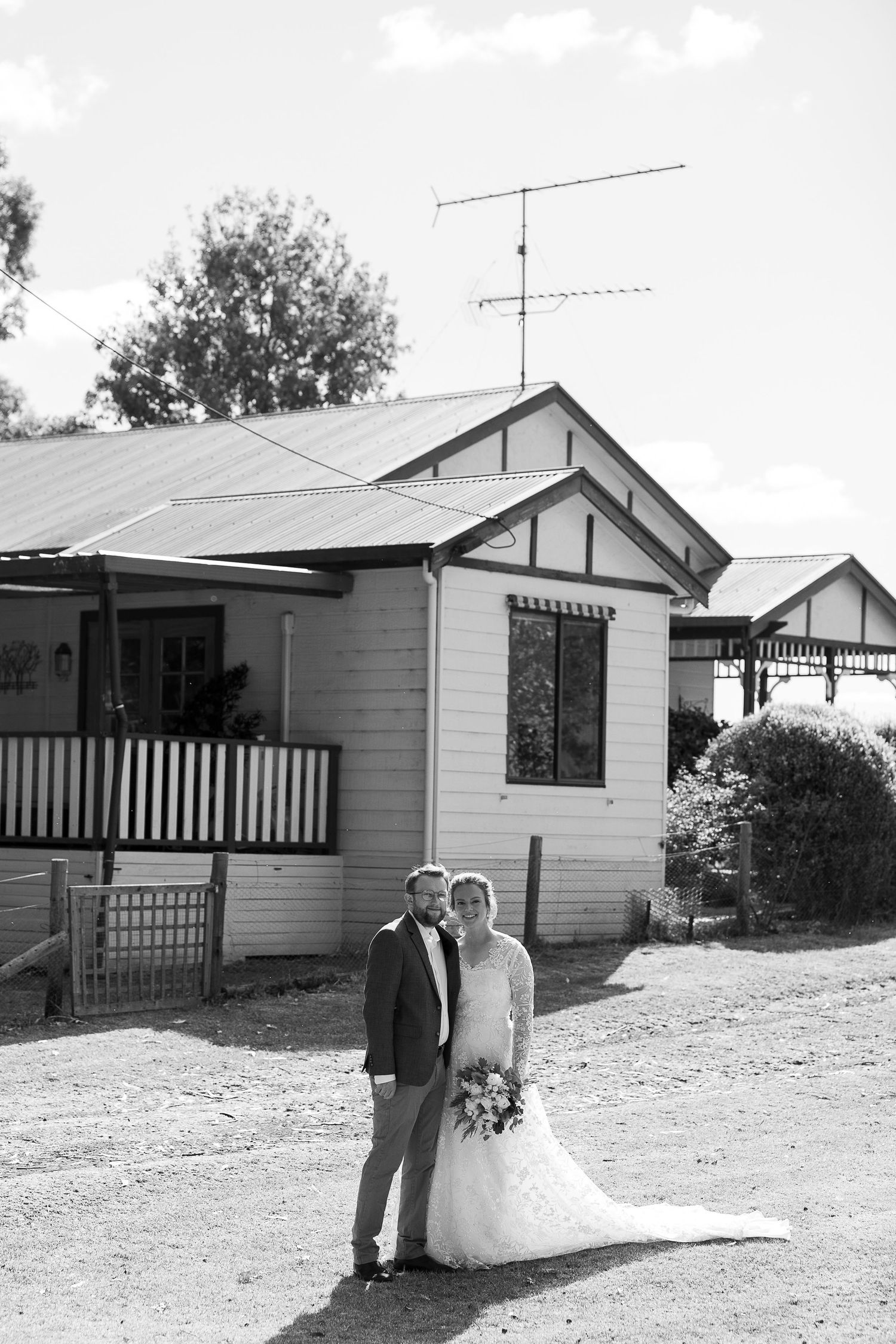 Wedding couple poses outside vintage cottage-style homes in black and white photography.