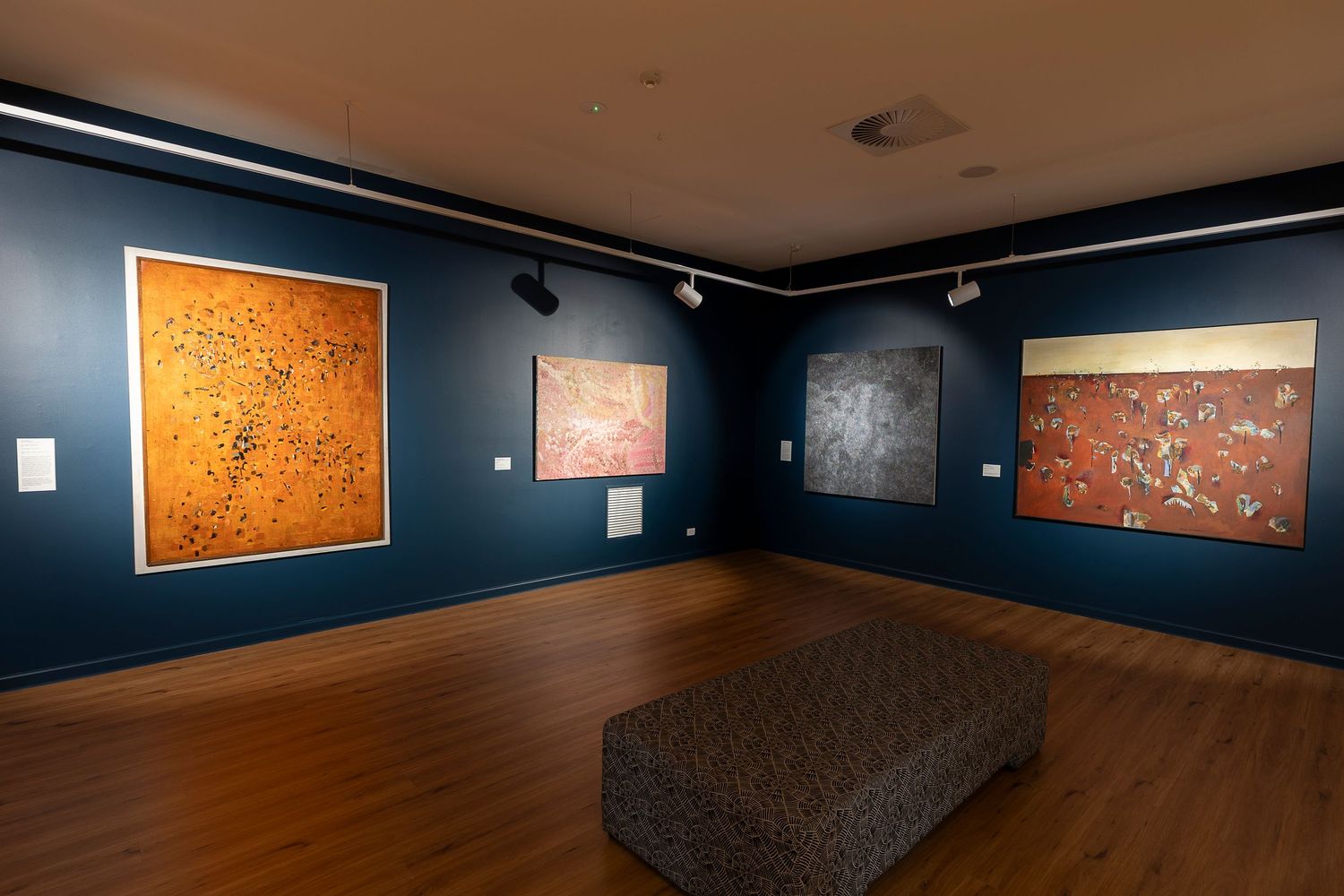 Museum gallery with dark blue walls showcasing large-scale contemporary paintings and installations.