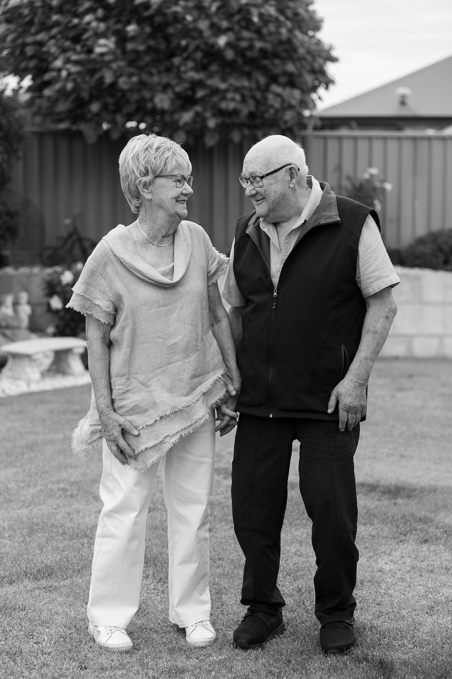 A black and white portrait of an elderly couple sharing a loving moment in their garden.
